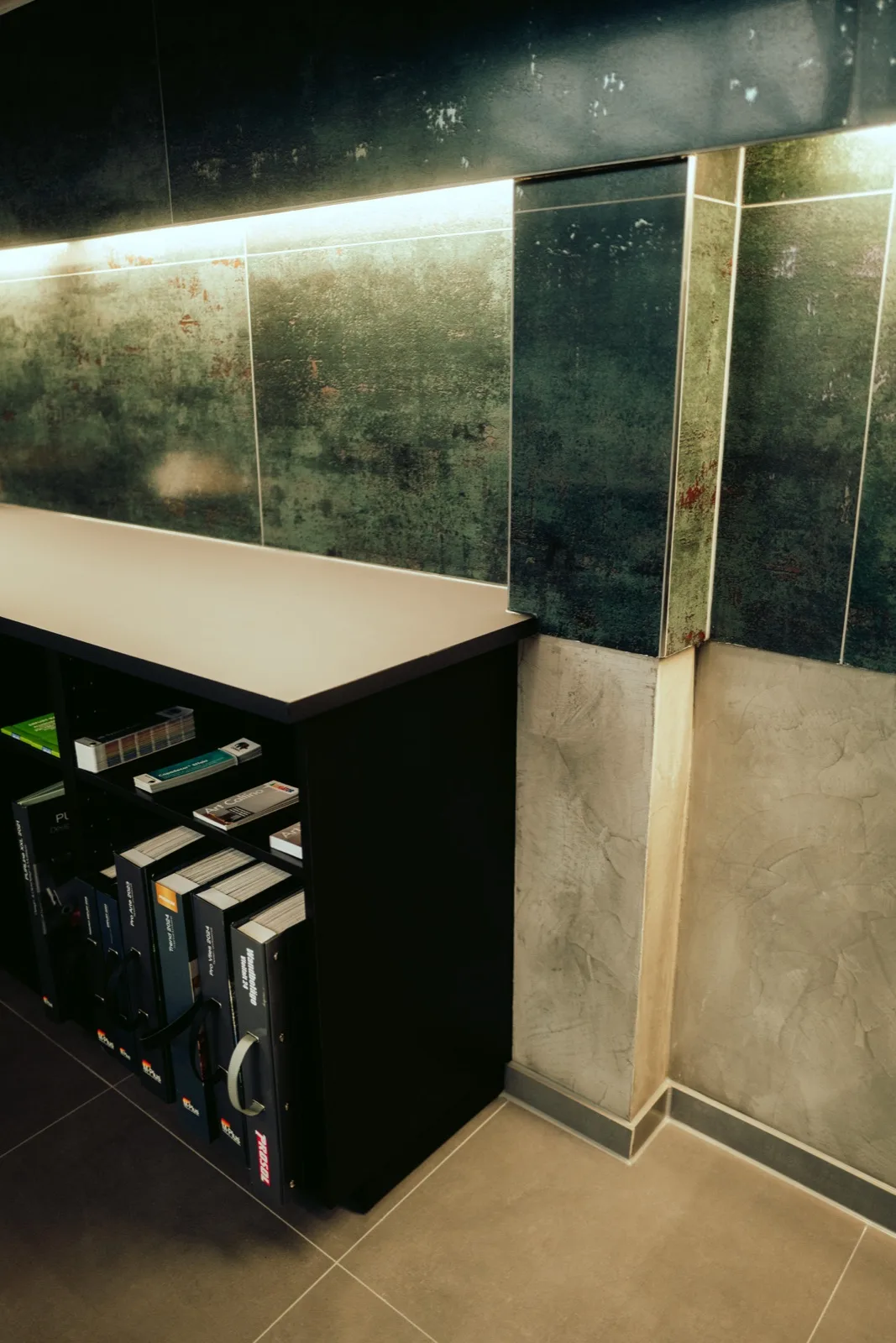 Showroom mit Fliesenmustern in Metalloptik an der Wand und Katalogordnern im Regal