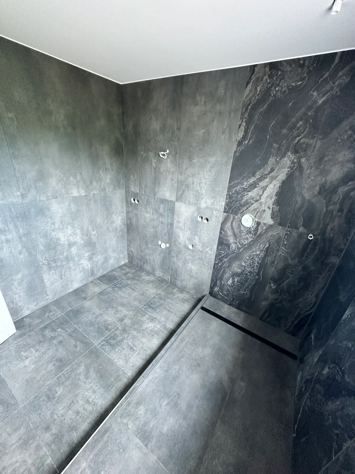Bodengleicher Duschbereich mit grauen Großformatfliesen, dunkler Marmoroptik-Wand und Duschrinne