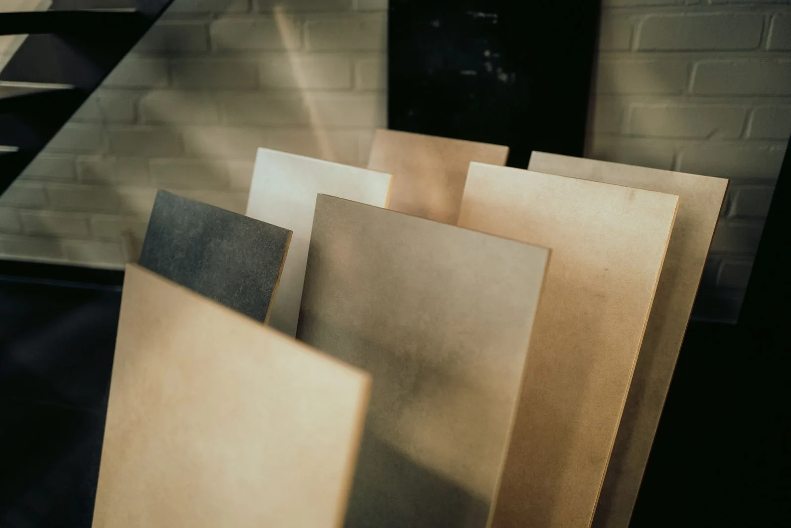 Feinsteinzeugplatten in Beige-, Sand- und Anthrazittönen vor einer weißen Backsteinwand im Showroom